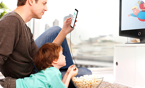 Vue d’un homme regardant un téléphone intelligent assis à côté d’un garçon regardant la télévision avec du maïs soufflé dans les mains.