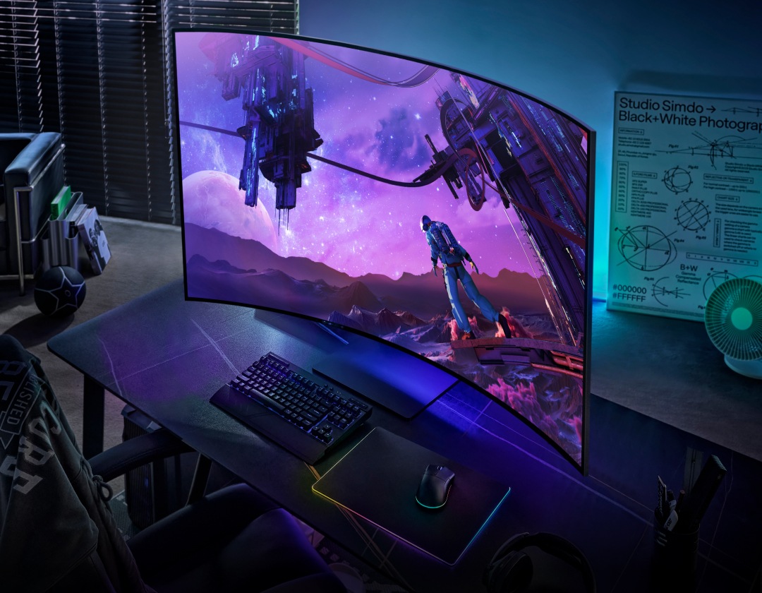 شاشة Odyssey Ark موضوعة على مكتب، ويظهر عليها رائد فضاء ينظر إلى محطتين فضائيتين من كوكب خارجي. تضفي أضواء الشاشة توهجاً على الغرفة. توجد فوق الشاشة شارة لجائزة CES Innovation Awards، والتي اختارت شاشة Odyssy Ark الشاشة الفائزة لعام 2022.