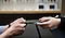 Closeup of the hands of a Galaxy Consultant handing a repaired phone in a case to the hands of a client across the counter