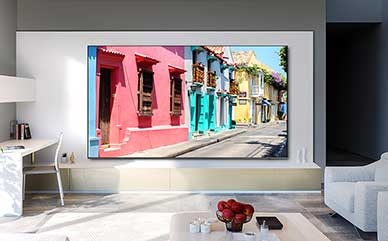 Un TV de pantalla grande de 98 pulgadas está colgado en la pared de una sala de estar y muestra edificios coloridos