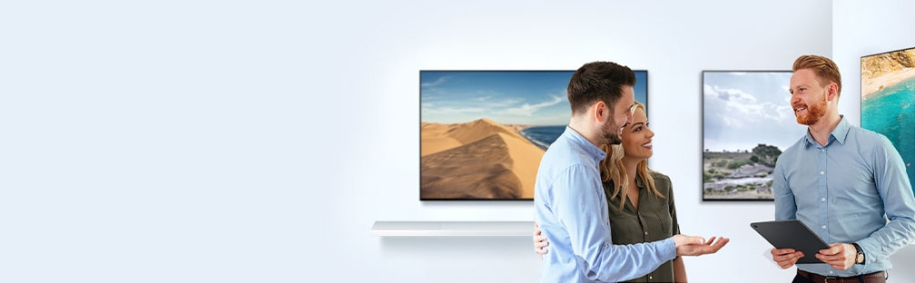Para comprar un  TV nuevo, un hombre y una mujer están hablando con un dependiente sobre las características de un TV en una tienda de TV.