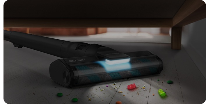 Hay una aspiradora Samsung Jet con el Cepillo Slim LED+ que llega hasta debajo del sofá para aspirar la suciedad. La iluminación LED está encendida.