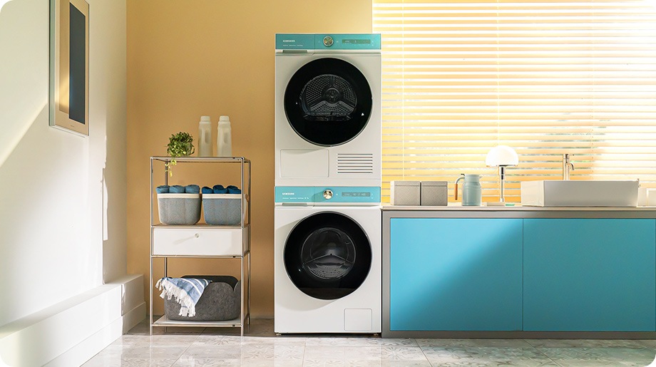 Há um conjunto de máquina de lavar e máquina de secar Bespoke AI™ em branco, com painéis na cor Morning Blue, ao lado de um armário azul com um lava-loiças. A máquina de secar está colocada em cima da máquina de lavar.