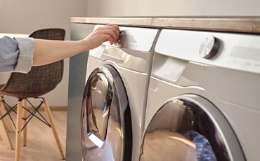 Siniseen takkiin pukeutunut nainen ohjaa Samsung-pyykinpesukonetta.