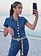 Une femme portant une combinaison en jean prend un selfie sur le sable d’une plage.