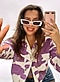 Une femme portant des lunettes de soleil blanches et une veste violette et blanche à imprimé vache prend un selfie miroir.
