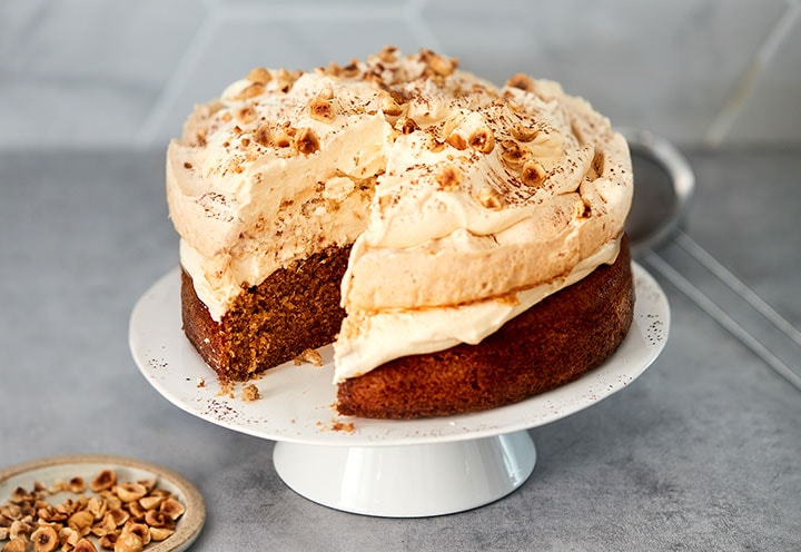 Une génoise au café recouverte de meringue aux noisettes et de crème fouettée dans une assiette blanche.