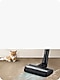 A cat is lying on the living room floor and a Samsung Cordless vacuums is cleaning the pet's fur in front of it.