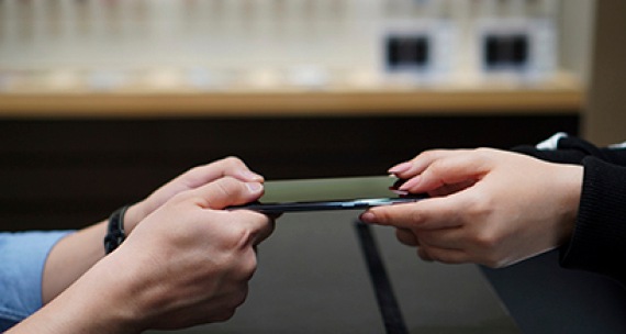 Plan rapproché des mains d'un Consultant Galaxy tendant un téléphone réparé à un client de l'autre côté du comptoir.