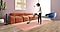 Une femme passe l'aspirateur sur un tapis rose avec un Bespoke JET dans un salon élégant. Une Clean Station intégrée se trouve à côté d'un canapé marron.
