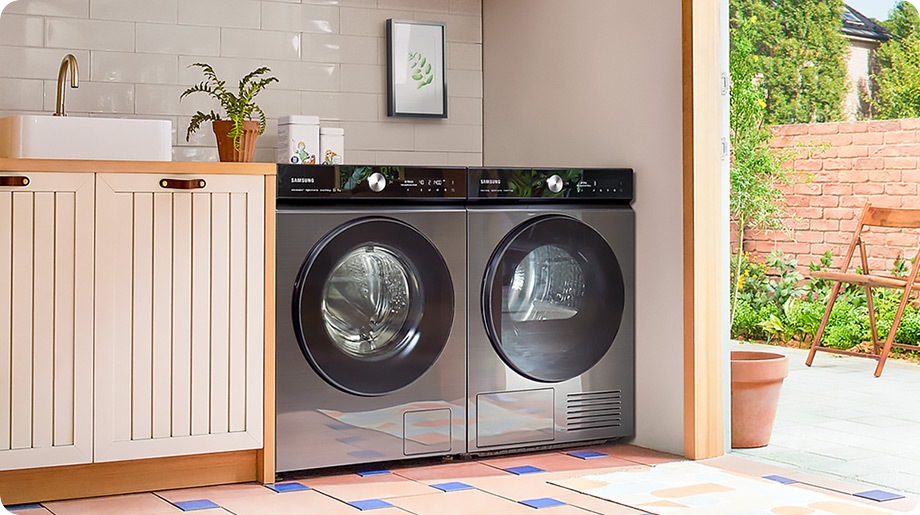 L'ensemble lave-linge et sèche-linge BESPOKE AI™ noir est placé dans une armoire en bois dans une pièce avec des murs beiges et un sol carrelé coloré.