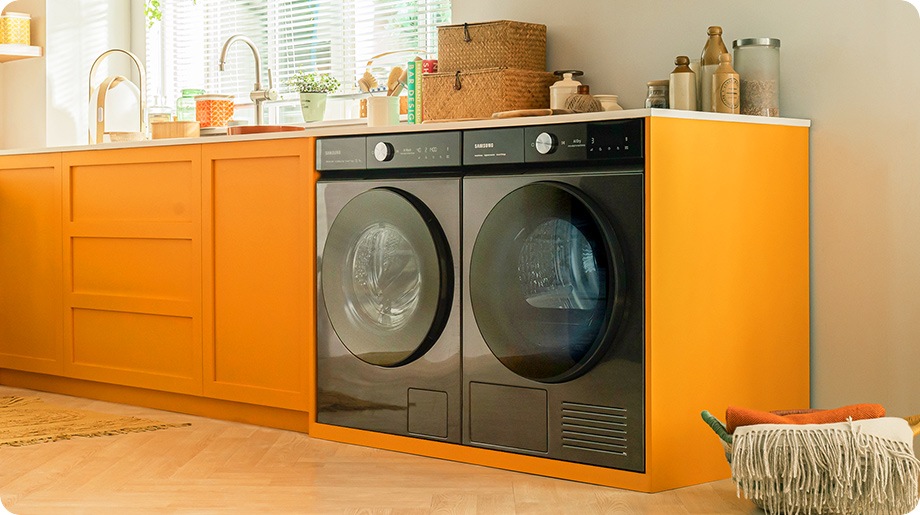 L'ensemble lave-linge et sèche-linge BESPOKE AI™ blanc est placé dans une armoire de couleur orange dans une cuisine confortable.