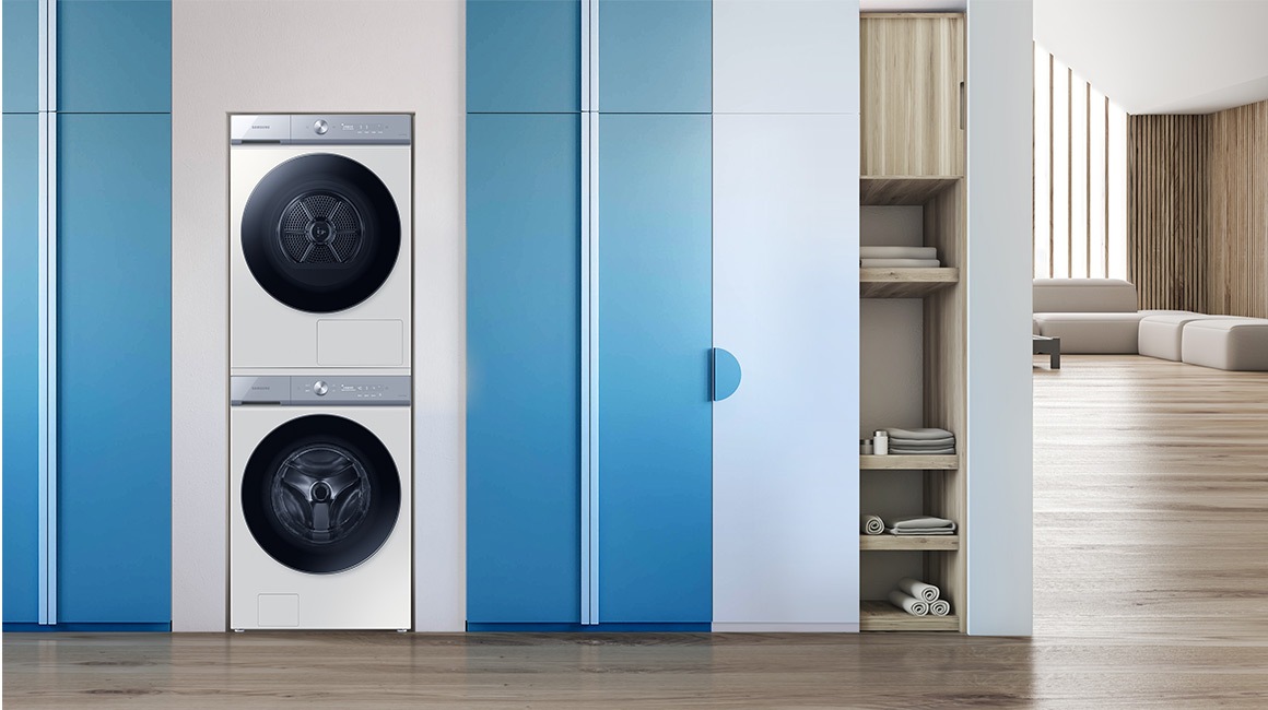 L’ensemble lave-linge et sèche-linge empilé est positionné entre une plante verte et un meuble à étagères.