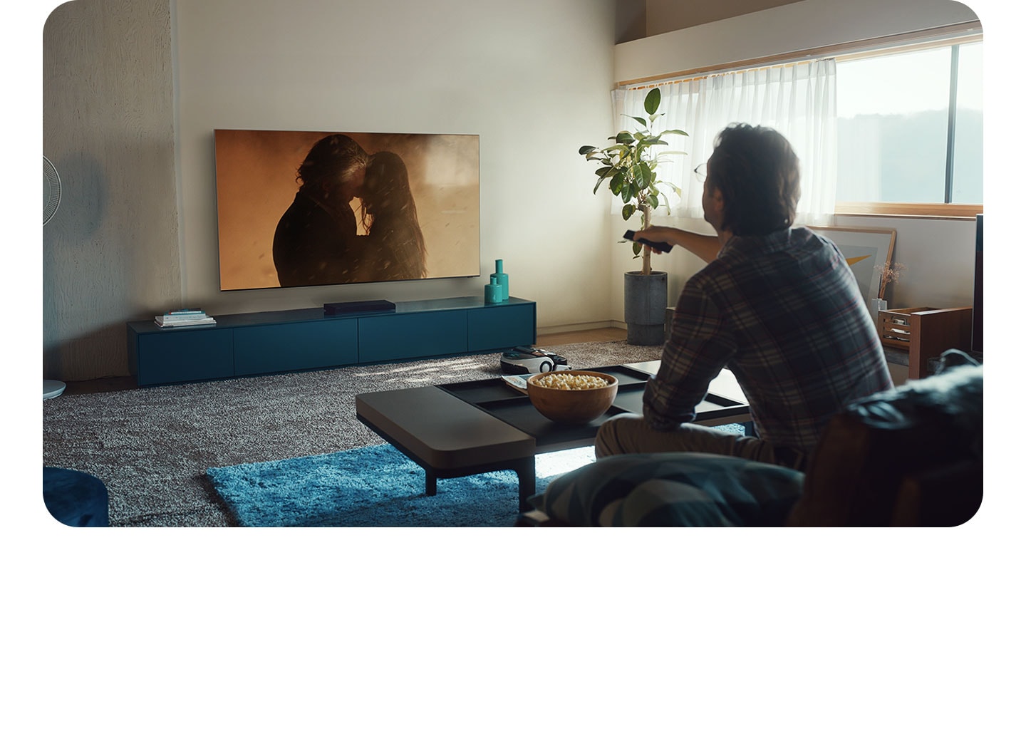 Video footage of several remote controls on a coffee table. A hand picks up one of the remotes and presses its buttons. Another hand is pressing buttons on a different remote. A little boy is rummaging through a box of remotes in search of the right one. Then text appears saying, having to look for different remotes isn't exactly ideal. With Samsung Smart TV, One Remote is all you need. We then see a hand holding the Samsung Smart TV One Remote and then see the person sitting on a couch using the One Remote to control the Samsung Smart TV and his coffee table is clear of any other remotes and he's smiling. Then the One Remote appears on a dark background with the text Samsung One Remote.