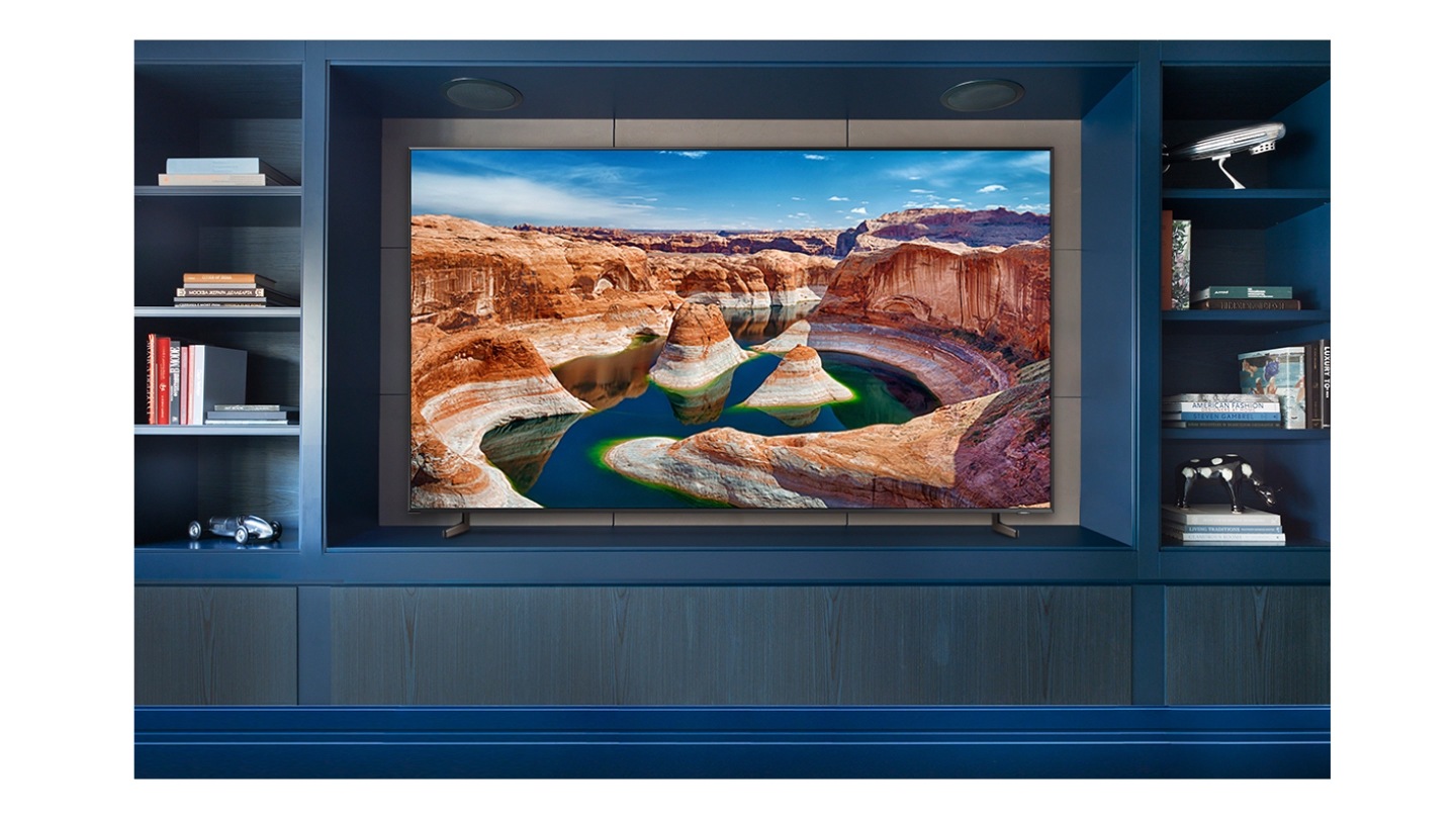 A Super Big TV is between two TV cabinets. On the TV screen is an overhead picture of a daytime desert canyon.