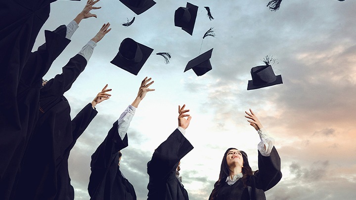 Επτά νέοι απόφοιτοι που πετούν τα καπέλα της αποφοίτησής τους στον αέρα.
