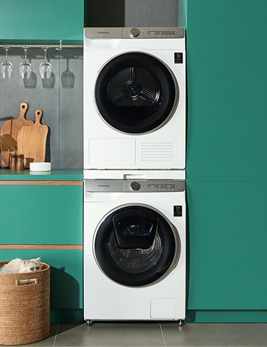 Ένα λευκό πλυντήριο και ένα στεγνωτήριο ρούχων από τη Samsung είναι τοποθετημένα στην κουζίνα με ένα πράσινο φόντο.