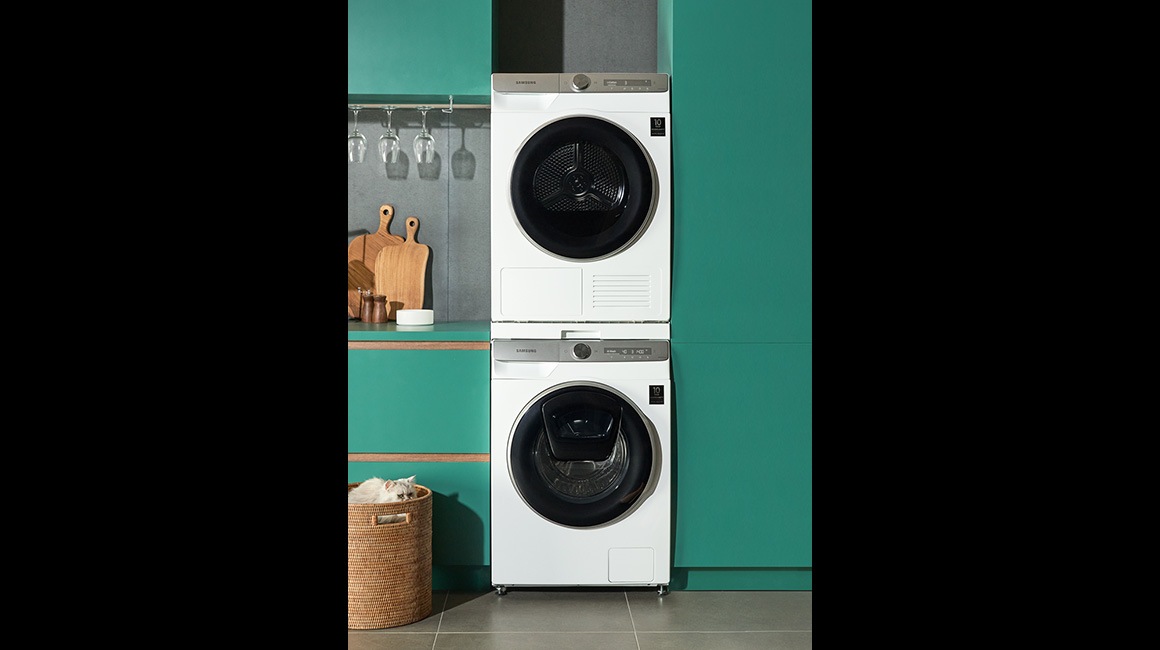 Ένα λευκό πλυντήριο και ένα στεγνωτήριο ρούχων από τη Samsung είναι τοποθετημένα στην κουζίνα με ένα πράσινο φόντο.