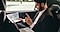 In the backseat of a car, a man in a suit is going through business papers in his hand with a Galaxy Book sitting on his lap.