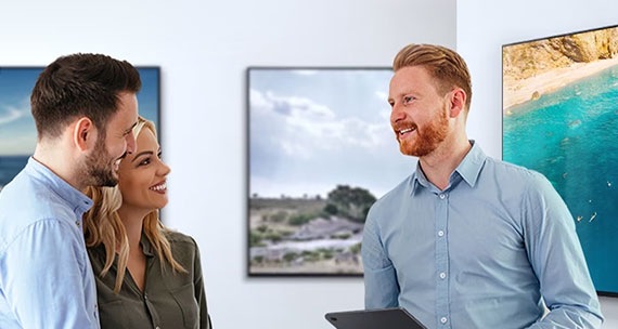 A couple consults a man about the different Samsung TVs that are displayed in the background.