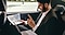 In the backseat of a car, a man in a suit is going through business papers in his hand with a Galaxy Book sitting on his lap.