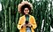 A woman with a bright coat and windblown hair stands in front of cacti and smiles at her Galaxy S21 Ultra.
