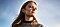 A woman in a grey sweater stands looking off into the distance.