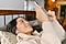 A lady lying on a bed in her home office, she is holding a phone and smiling at the content on the screen