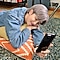 RM iz grupe BTS leži na jastucima na podu, trbuhom okrenutim prema dolje, oči su mu zatvorene i drži Galaxy S20 ispred sebe