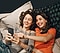 Two women lying down together smiling and looking at their smartphones.