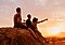 A family, sitting freely on the rocks, is appreciating the beauty of nature while they watch sunset on a distant mountain.