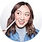 A studio headshot of Amanda Rach Lee wearing a denim jacket over a grey turtleneck sweater. She is holding a pink marker to her right cheek and looking off to the right, smiling.