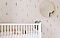 A baby in a white crib in a room with plant wallpaper and a circular mirror.