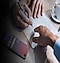 A hand with a pen is shown writingin a book. Another hand points to the words. To the left is a Samsung smartphone
