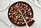 Chocolate tart topped with mashed nuts on it is on a white table.