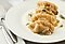 Steamed dumplings drizzled with butter and seasoned with black pepper and chives are on an white plate.
