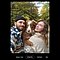 A viewfinder smartphone screenshot of a bearded man in a colourful blue coat while he takes a family selfie also featuring his brown dog and a young woman in a white knit sweater on a peaceful forest road bordered by beautiful autumn foliage.
