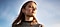 A woman in a grey sweater stands looking off into the distance.