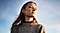 A woman in a grey sweater stands looking off into the distance.