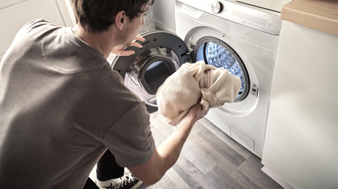 A man is putting the laundry in the Samsung white washing machine.