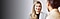 A woman stands in front of a blurry background shaking hands with another woman who is out of focus in the foreground.