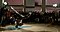In the center circle of a breakdance competition, a breakdancer is doing a head spin while the surrounding crowd and his opponent watch him.