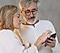زوجان كبيران في السن يرتديان ملابس بيضاء. وكلاهما ينظر إلى شيء ما ويفحصه على هاتف Galaxy الذكي الذي يحمله الرجل.