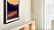 Inside a brightly lit living room, The Frame TV is seen from a side closeup and is hung using its wall mount option. There is an image of a sunset mountain scene on the screen.