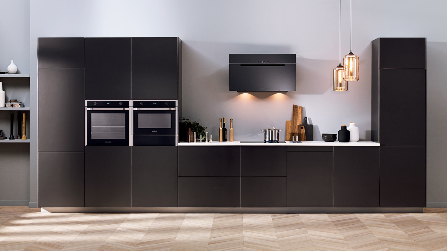 Un intero set di elettrodomestici da incasso Samsung come frigoriferi, forni, forni compatti, piani cottura, lavatrici e cappe installati in una cucina grigio scuro premium.