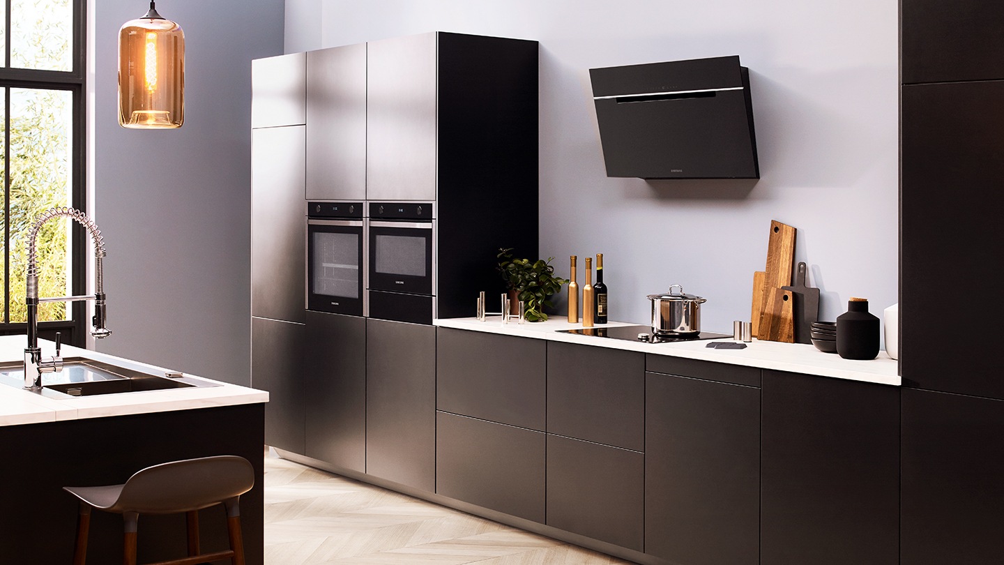 In una cucina grigio scuro premium sono installati un set di elettrodomestici da incasso Samsung come frigoriferi, forni, forni compatti, piani cottura, lavatrici e cappe.