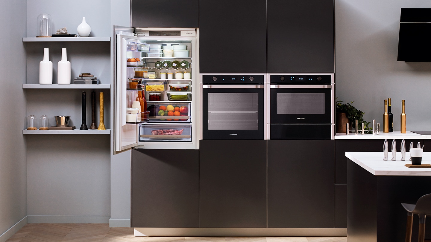 Un frigorifero da incasso Samsung con la porta aperta è installato in una cucina con i mobili neri.