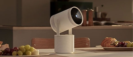 Il proiettore è appoggiato su un tavolo accanto a piatti pieni di cibo. L’emissione di luce indica che sta trasmettendo dei contenuti.