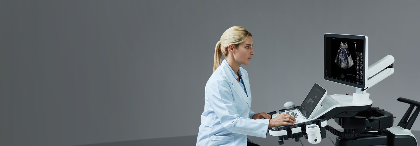 白衣を着た若い女性が、サムスンの携帯型超音波診断装置を操作している。画面には胎児の画像が映し出されている。