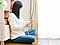 女性が床に座っている。女性は左手にスマートフォン、右手に充電ケーブルを持っている。